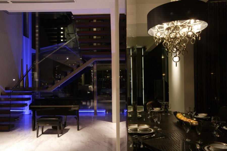 Double-height living room with a crystal chandelier and floating staircase lit in blue, Ocean Drive landed house