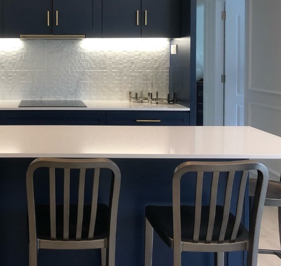 Navy shaker kitchen with brass handles, textured white backsplash and a quartz island with metal bar stools